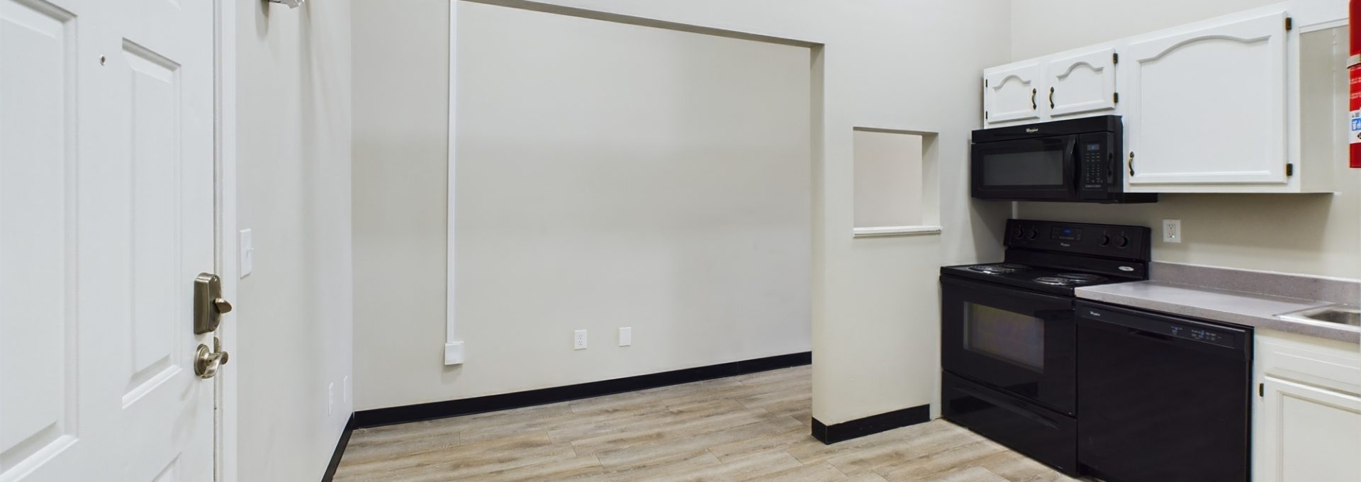 a kitchen with white cabinets and black appliances at The Kensington Apartments