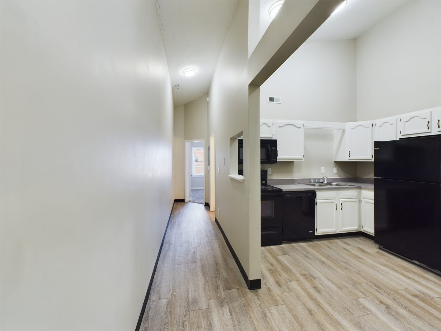 a long hallway with white walls and black appliances at The Kensington Apartments