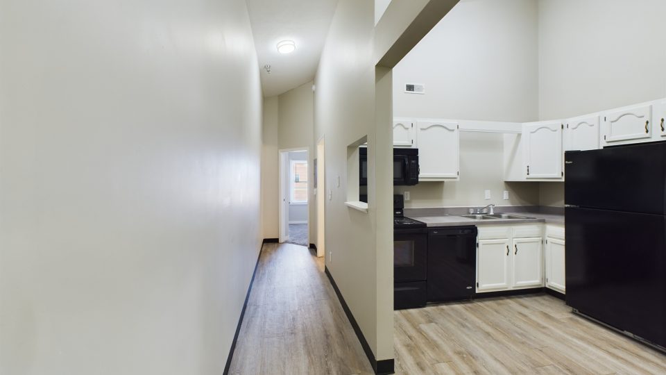 a long hallway with white walls and black appliances at The Kensington Apartments